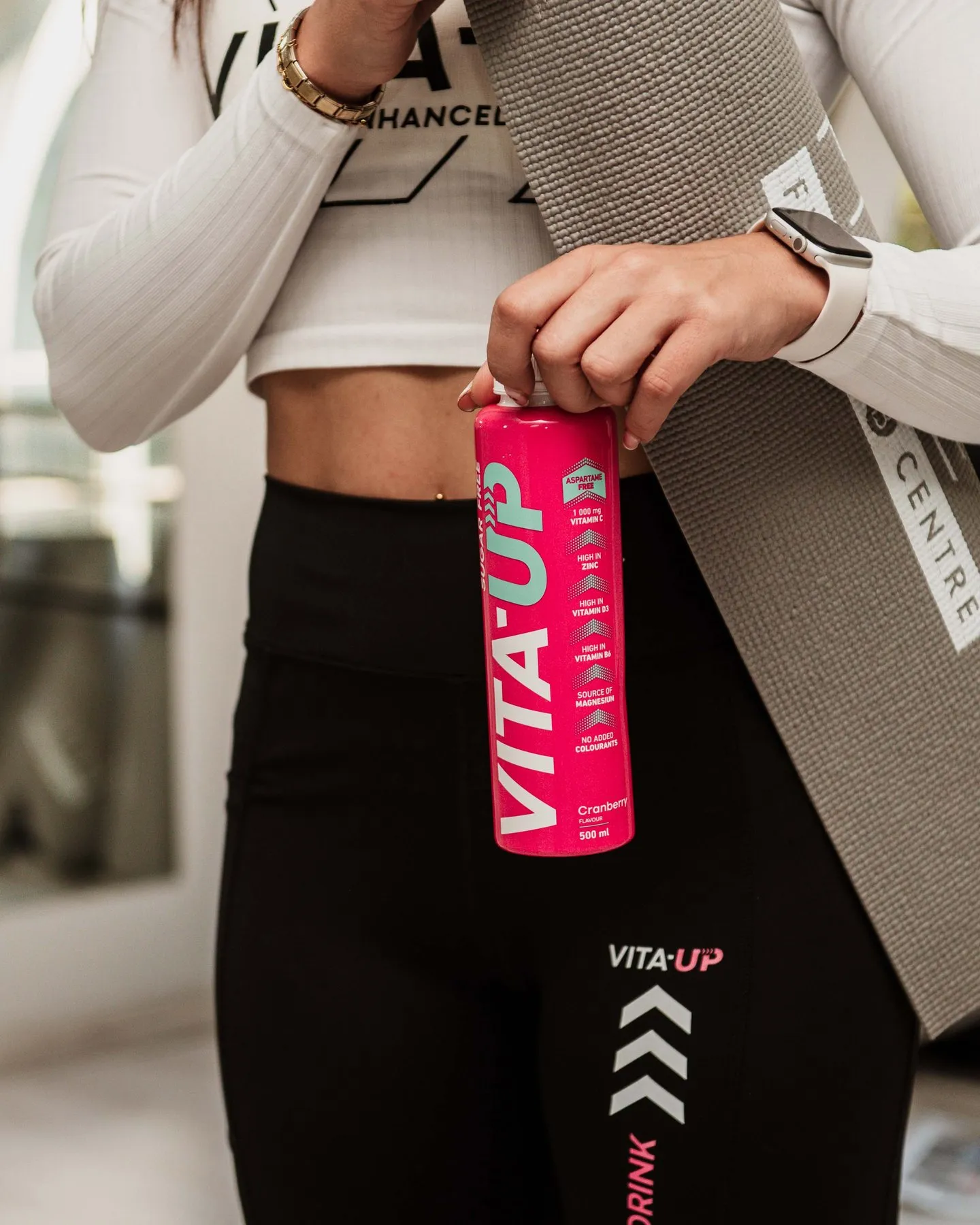 Woman with a yoga mat twisting open a Cranberry bottle